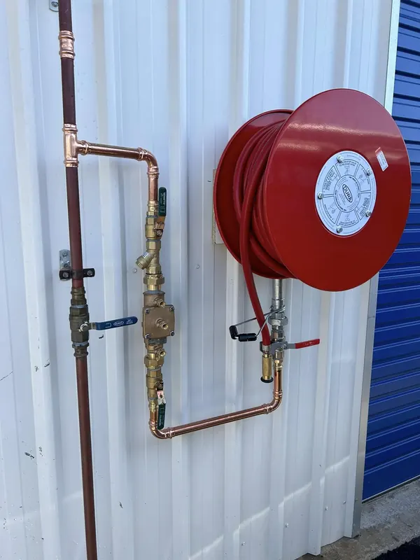 Backflow prevention device and fire hose reel installed on a commercial wall