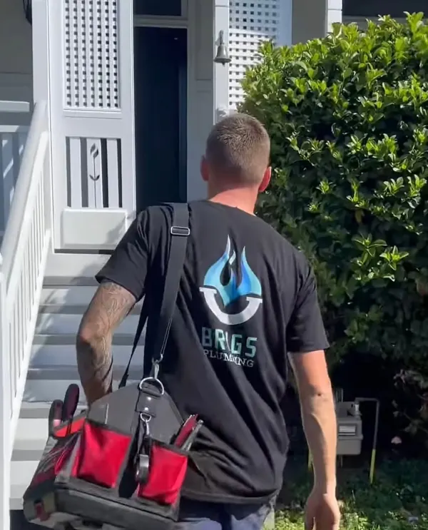 Niles arriving at a job in a Brigs Plumbing shirt with his tool bag
