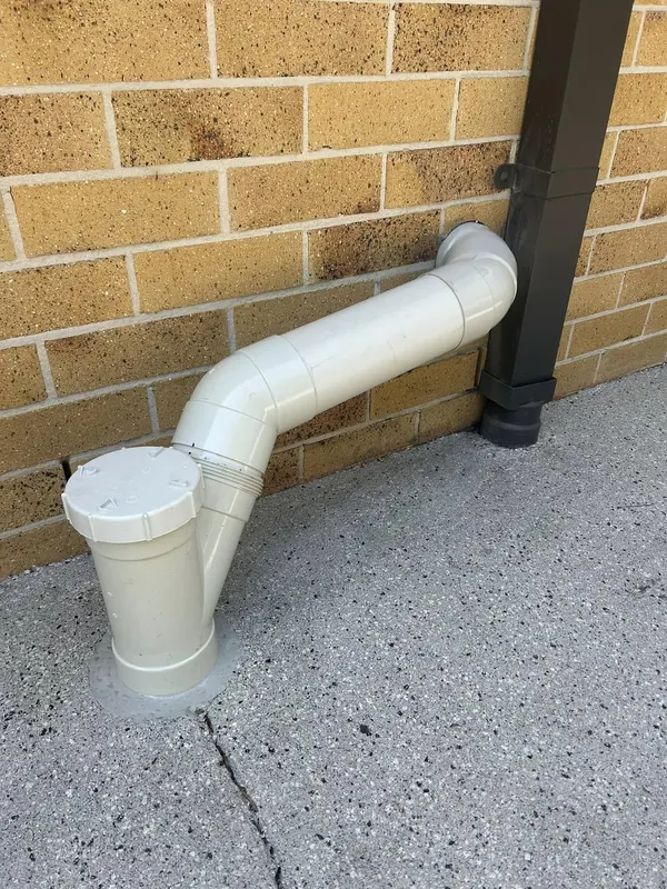 New PVC downpipe and rainhead installed against a brick wall