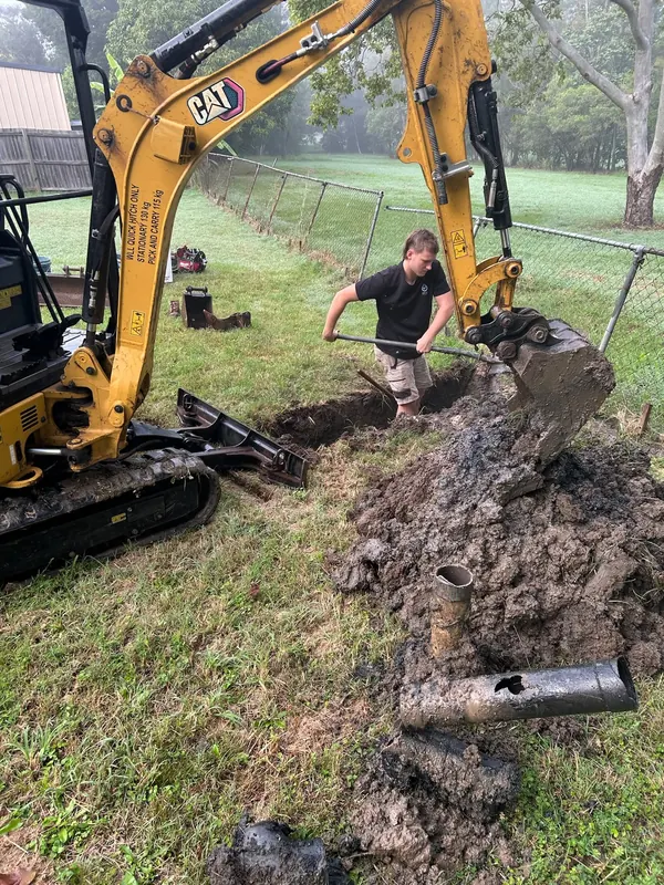 Excavator and plumber replacing a failed underground drain line