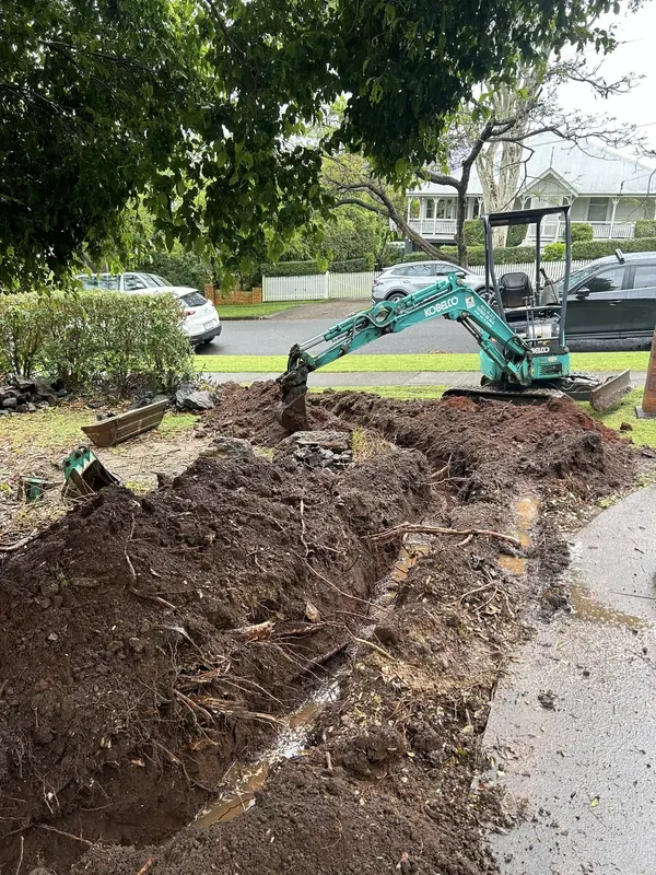 Mini excavator opening a trench in a front yard to reach a damaged drain