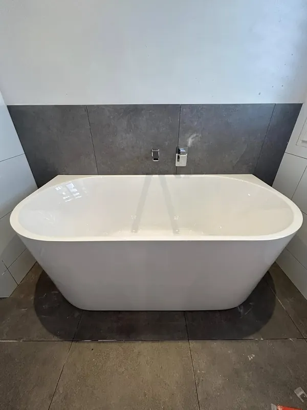 Freestanding bath installed and connected against a tiled feature wall