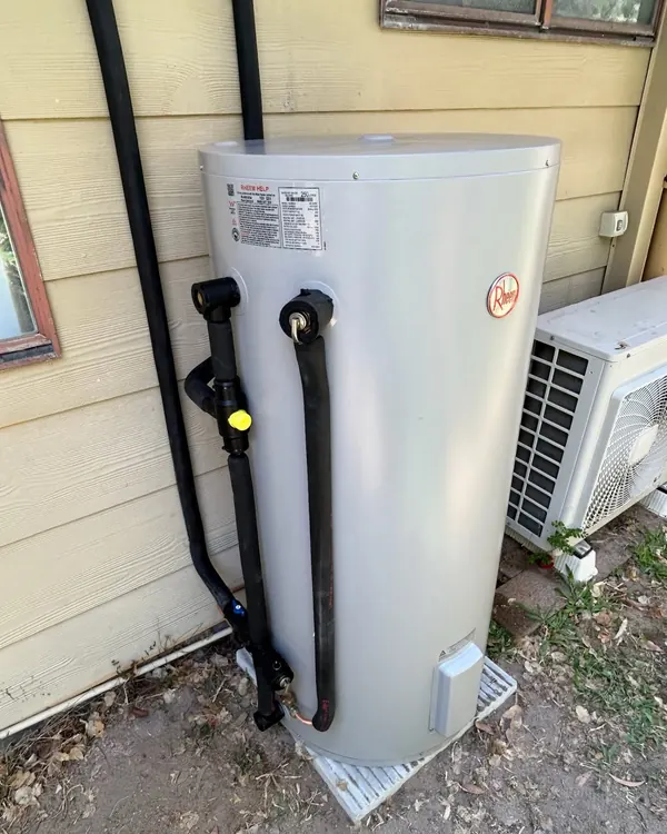 Replacement domestic hot water cylinder installed against a weatherboard wall