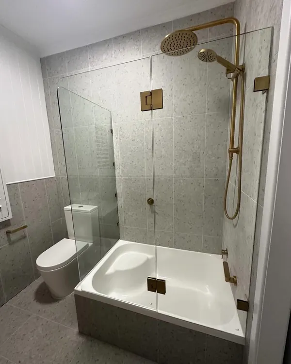 Finished bathroom with a shower over bath, glass screen and brass fittings