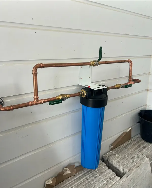 Whole-house water filter housing plumbed into copper pipework on an external wall